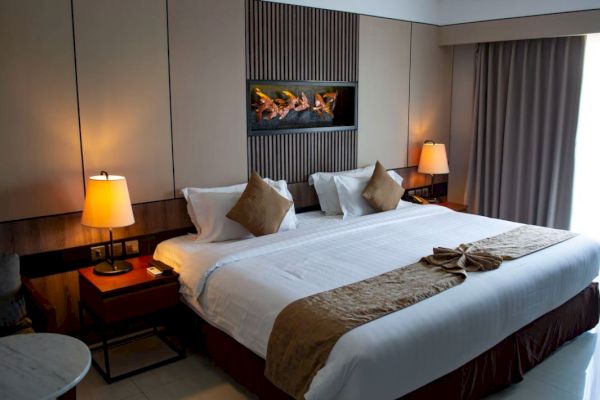 A cozy hotel room with a large bed, decorative pillows, bedside lamps, a small table, wall art, and drawn curtains in a modern setting.