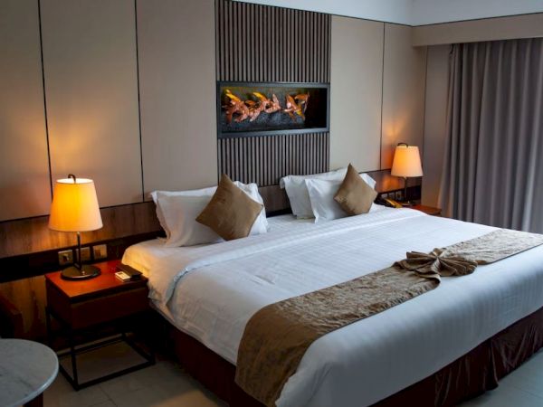 A cozy hotel room with a large bed, decorative pillows, bedside lamps, a small table, wall art, and drawn curtains in a modern setting.