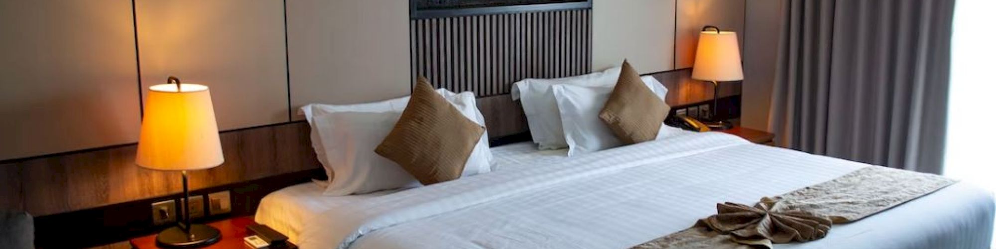 A well-decorated hotel room featuring a king-size bed with brown and white bedding, bedside lamps, and a decorative wall feature.