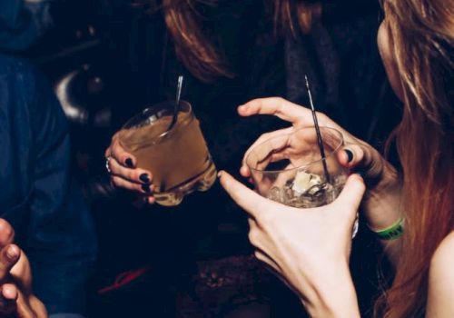 A group of people socializing and holding drinks. The image includes two visible drinks with straws and the people appear to be laughing and enjoying themselves.