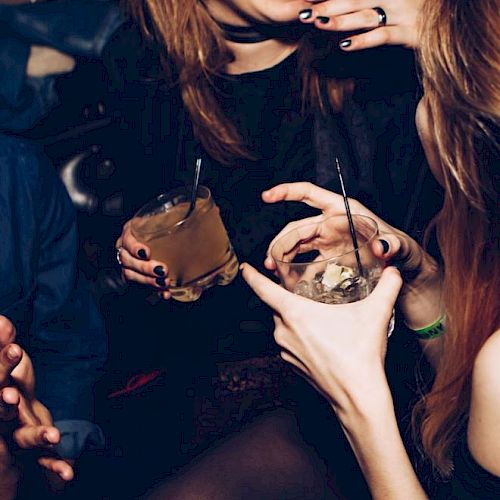 A group of people socializing and holding drinks. The image includes two visible drinks with straws and the people appear to be laughing and enjoying themselves.