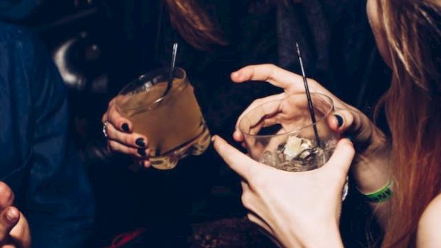 A group of people socializing and holding drinks. The image includes two visible drinks with straws and the people appear to be laughing and enjoying themselves.