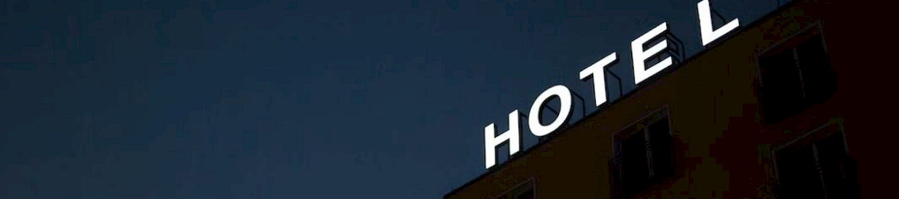 A building with a partially illuminated "HOTEL" sign at night, with the "E" missing a part of its light, against a dark sky.