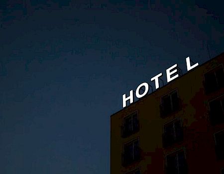 A building with a partially illuminated "HOTEL" sign at night, with the "E" missing a part of its light, against a dark sky.