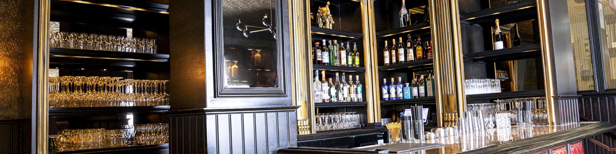 An elegant bar with red upholstered stools, shelves of glasses, bottles of liquor, a gold ceiling, and black walls.