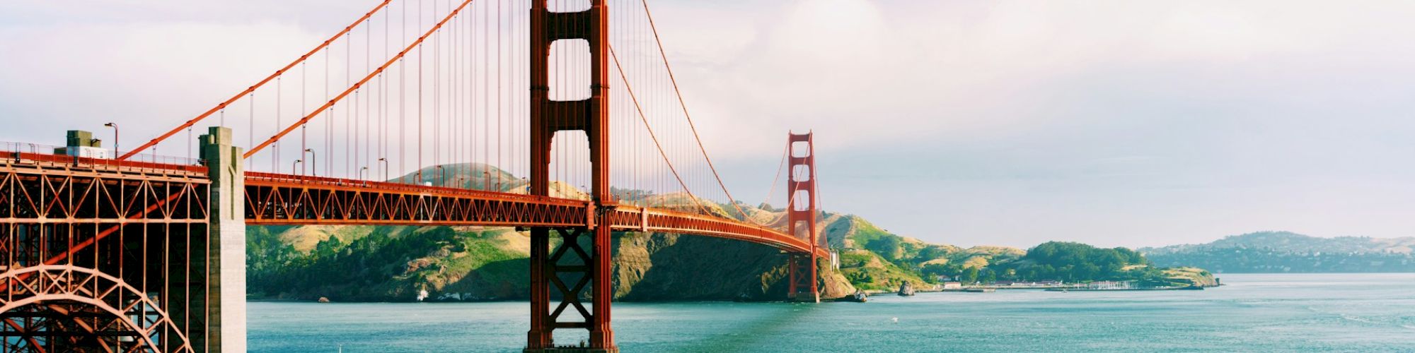 This image features the iconic Golden Gate Bridge spanning over a body of water with a fort structure in the foreground and scenic hills in the background.