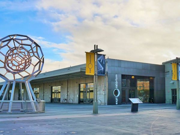 The image shows a modern building with geometric sculpture outside and yellow banners on poles. The building has signs that read "aquarium".