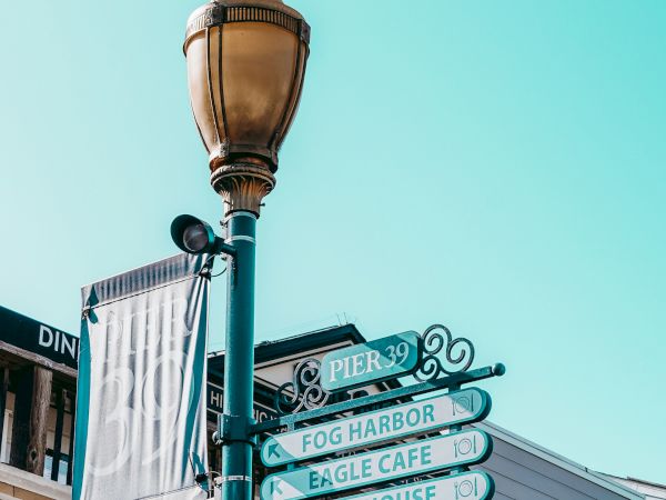 The image features a street lamp post with directional signs in front of shops, set against a clear blue sky.