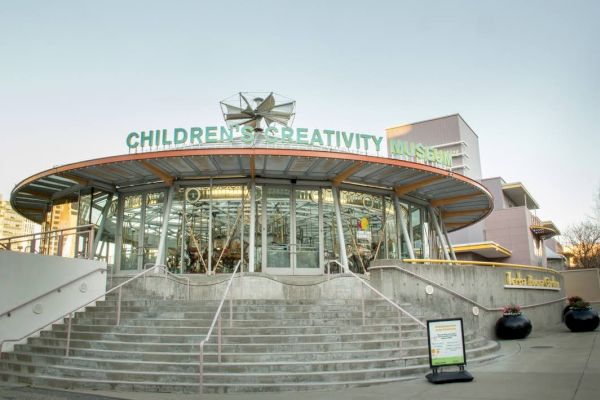 The image shows the exterior of the Children's Creativity Museum building with stairs leading up to the entrance, featuring a carousel inside.