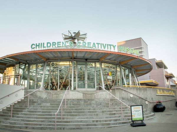 The image shows the exterior of the Children's Creativity Museum building with stairs leading up to the entrance, featuring a carousel inside.