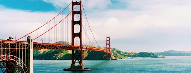 A scenic view of the Golden Gate Bridge spanning over a body of water, with a clear sky and rolling hills in the background.