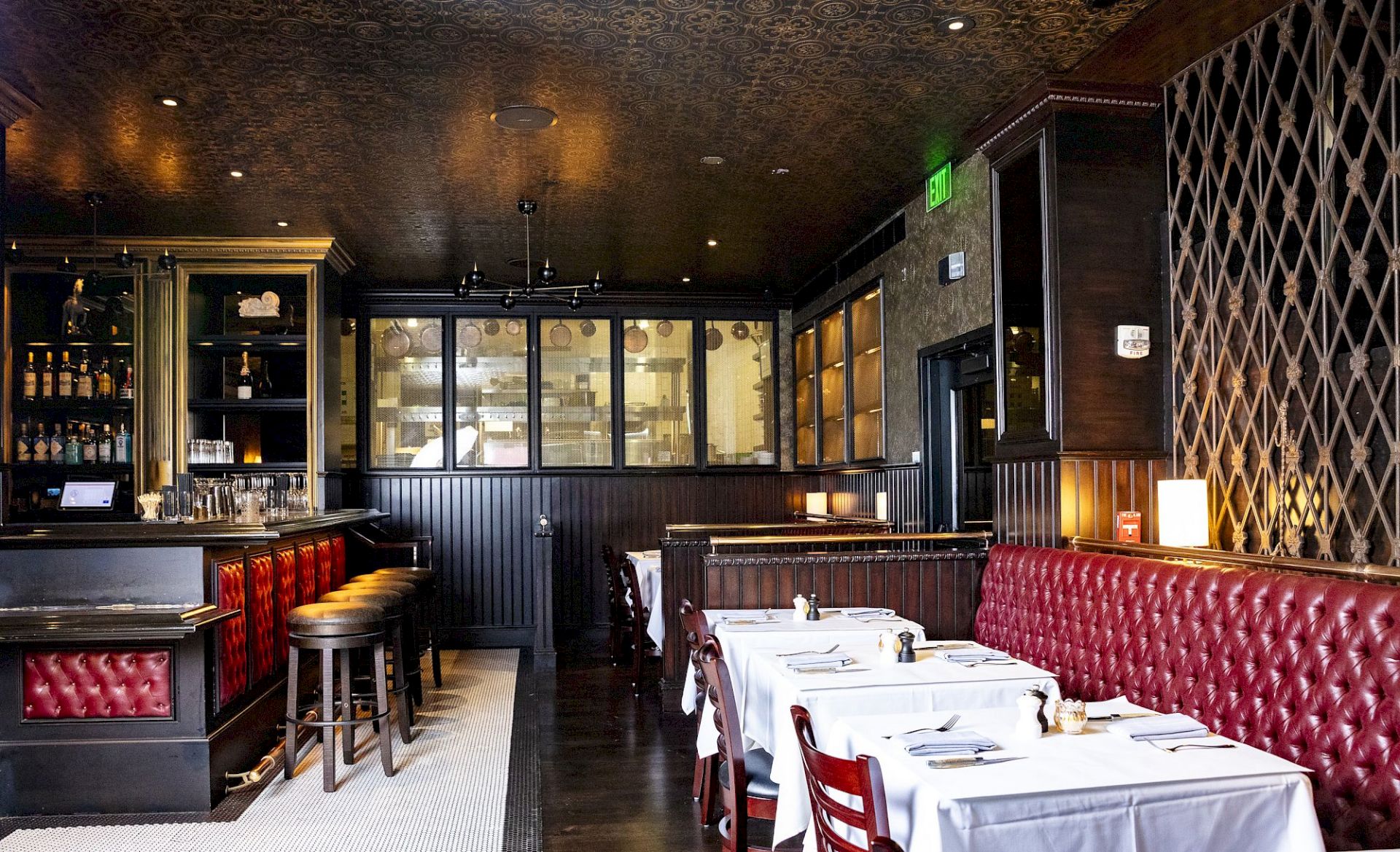 The image shows a stylish restaurant interior with red leather seating, white tablecloths, and a bar area with stools and shelves.