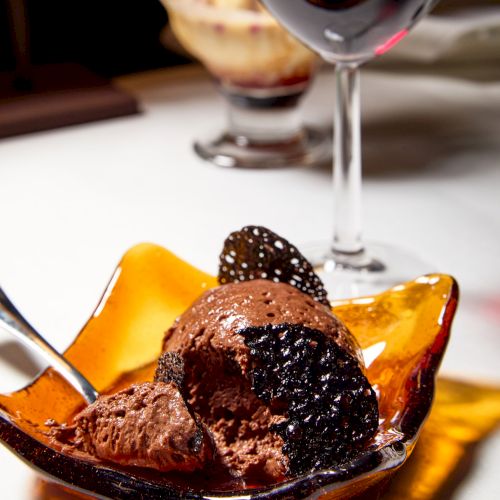 Dessert plate with chocolate and brownie-like scoops drizzled with sauce, with a martini glass in the background.