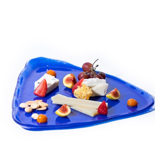 A blue triangular plate with various cheeses, figs, grapes, strawberries, and small pastries arranged artistically on it.