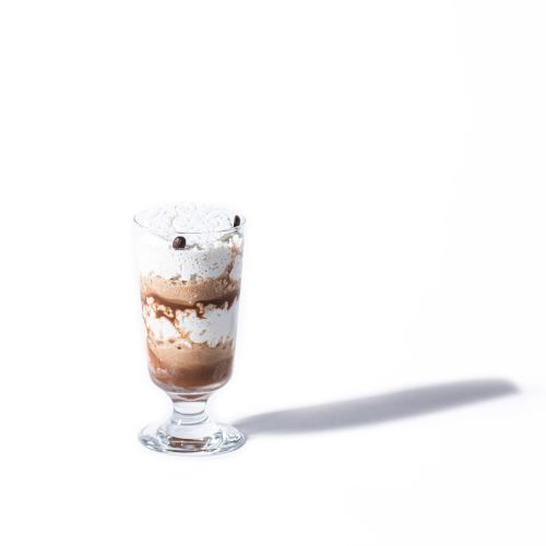 The image shows a layered dessert in a glass, possibly a parfait or sundae, with chocolate, cream, and topped with small garnish pieces.