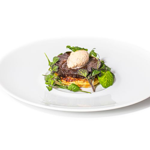 The image shows a plated dish with a slice of toasted bread, leafy greens, and a scoop of creamy topping on a white plate.