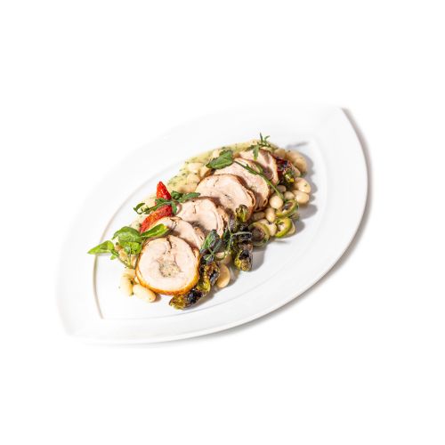 The image shows a plated dish of sliced stuffed chicken breast, garnished with herbs, chili, and served with a side of sautéed vegetables.