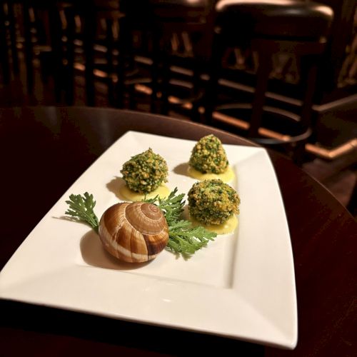 A plated serving of escargot with garlic-herb butter and parsley beside three green herb-coated bites, in a cozy grill/fireplace setting.