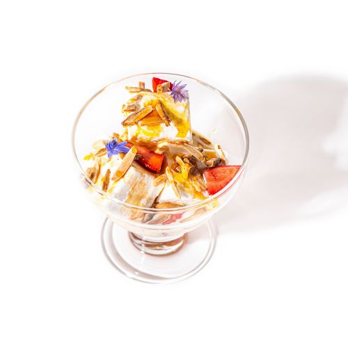 This image shows a dessert bowl containing a mix of fruits, colorful flower petals, possibly nuts, and a creamy base.