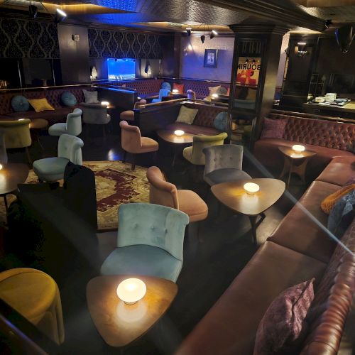 A cozy bar/lounge with velvet seating, small round tables, and blue neon light.
