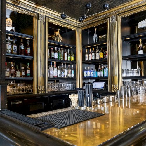 This image shows a well-stocked bar with various bottles of alcohol, glassware, and a polished bar counter, enclosed in a luxurious setting.