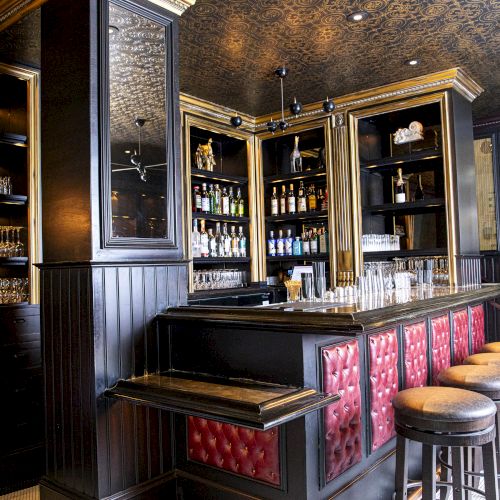 This image shows a chic bar interior with a high ceiling, shelves of glassware and bottles, black and red decor, and several barstools lined up.