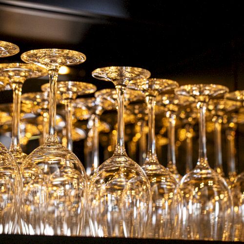 The image shows several rows of upside-down wine glasses arranged neatly on a shelf or rack, reflecting light beautifully.