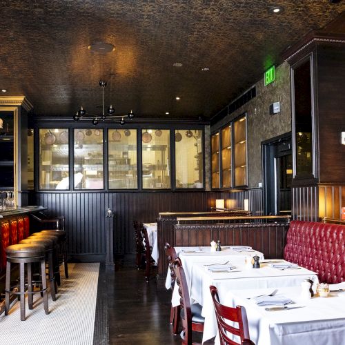 The image shows a cozy restaurant interior with red leather seating, white tablecloths, a well-stocked bar, and warm lighting.