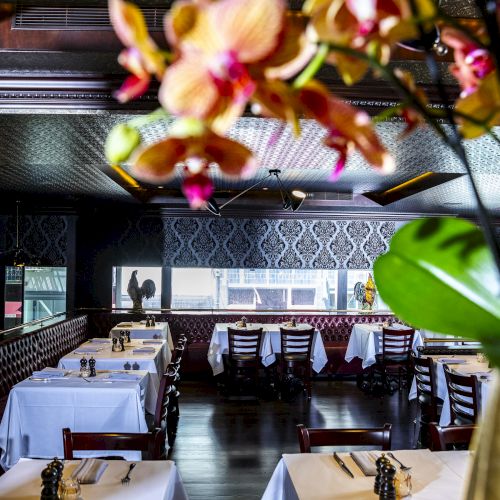 The image depicts a beautifully decorated restaurant with elegant table settings, white tablecloths, ornate wallpaper, and vibrant flowers in the foreground.