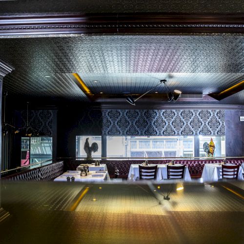 This image shows a luxurious restaurant interior featuring table settings, elegant wallpaper, mirrored surfaces, and upholstered seating.