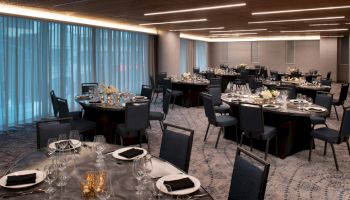 The image shows an elegant dining or event room with round tables set with black tablecloths, glassware, and decorations, and surrounded by chairs.