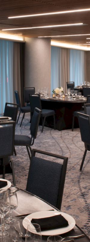 The image shows a banquet hall set up with round tables and chairs, featuring elegant table settings with glassware, napkins, and centerpieces.