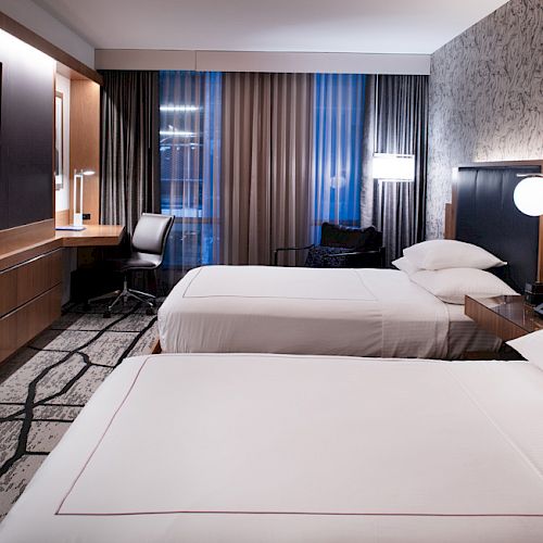 The image shows a modern hotel room with two beds, a desk and chair by the window, a large flat-screen TV on the wall, and contemporary decor ending the sentence.