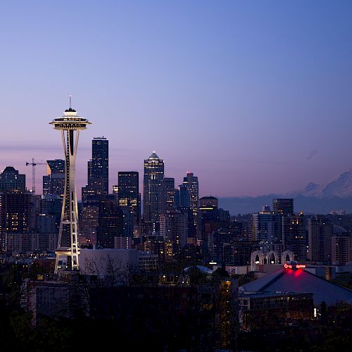 The image shows the Seattle skyline at dusk, featuring the Space Needle, downtown buildings, and Mount Rainier in the background, under a twilight sky.