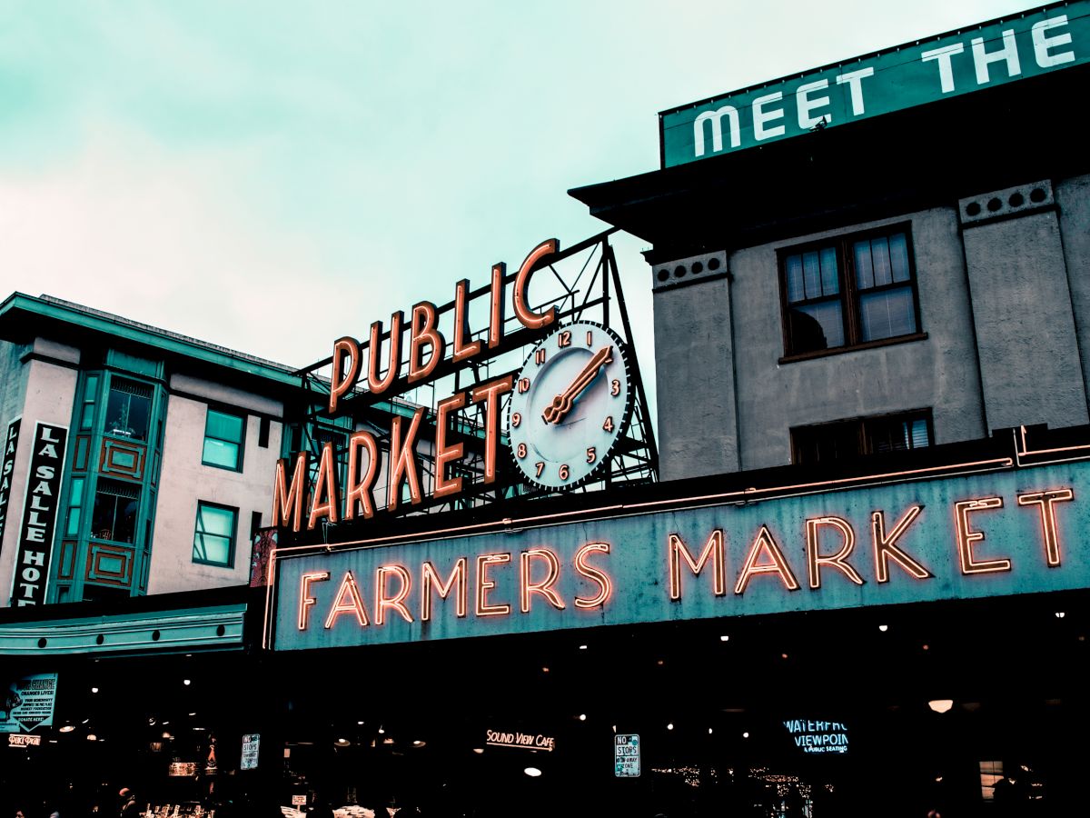 The image shows a famous public market with neon signs reading "Public Market" and "Farmers Market," along with a clock.