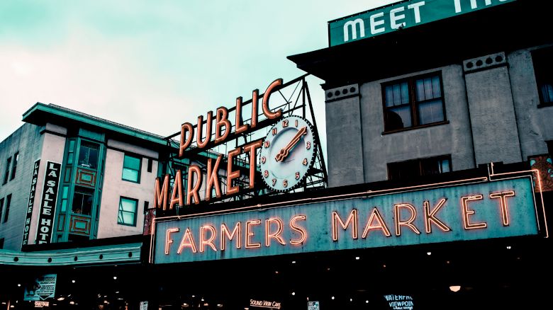 The image shows a famous public market with neon signs reading "Public Market" and "Farmers Market," along with a clock.