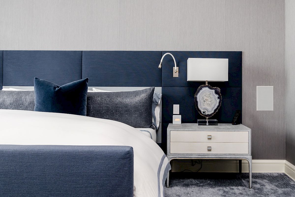 A modern bedroom with a blue and white color scheme, featuring a bed, side table with lamp, and decorative pillows on the bed, ending the sentence.